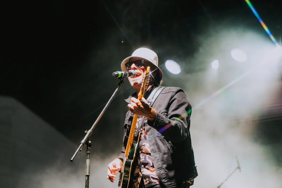 Close-up of musician singing into microphone wearing white bucket hat with atmospheric stage fog